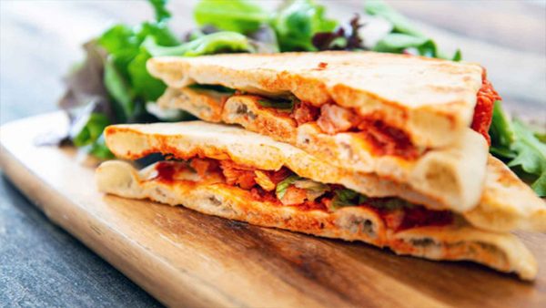 A chicken sandwich with a side of salad on a wooden serving board.