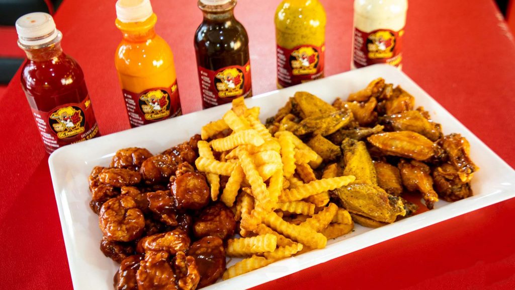 A platter of 6 buffalo strips with french fries accompanied by various sauces.