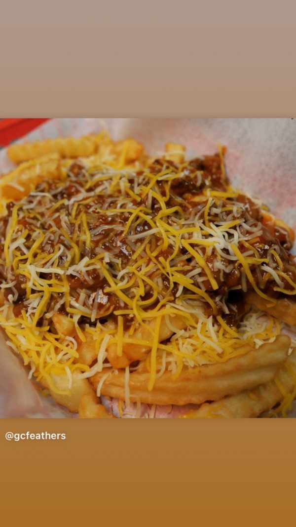 Plate of waffle fries topped with shredded cheese and chili sauce.