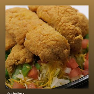 Fried chicken tenders served over a bed of salad with shredded cheese and diced tomatoes.