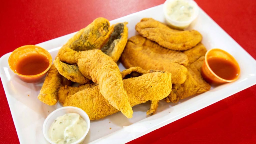 A platter of fried fish served with dipping sauces.
