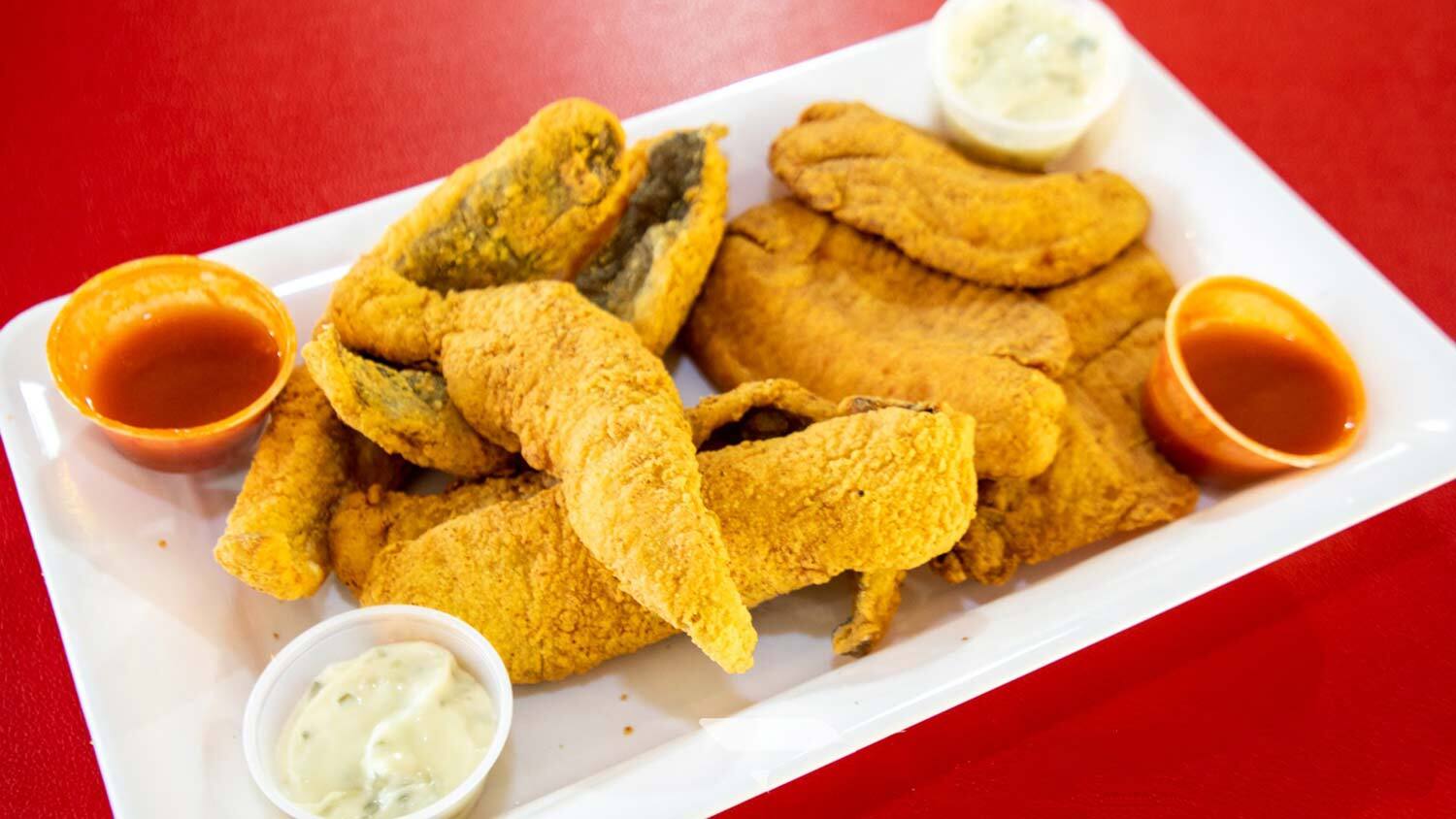 A platter of fried fish served with dipping sauces.