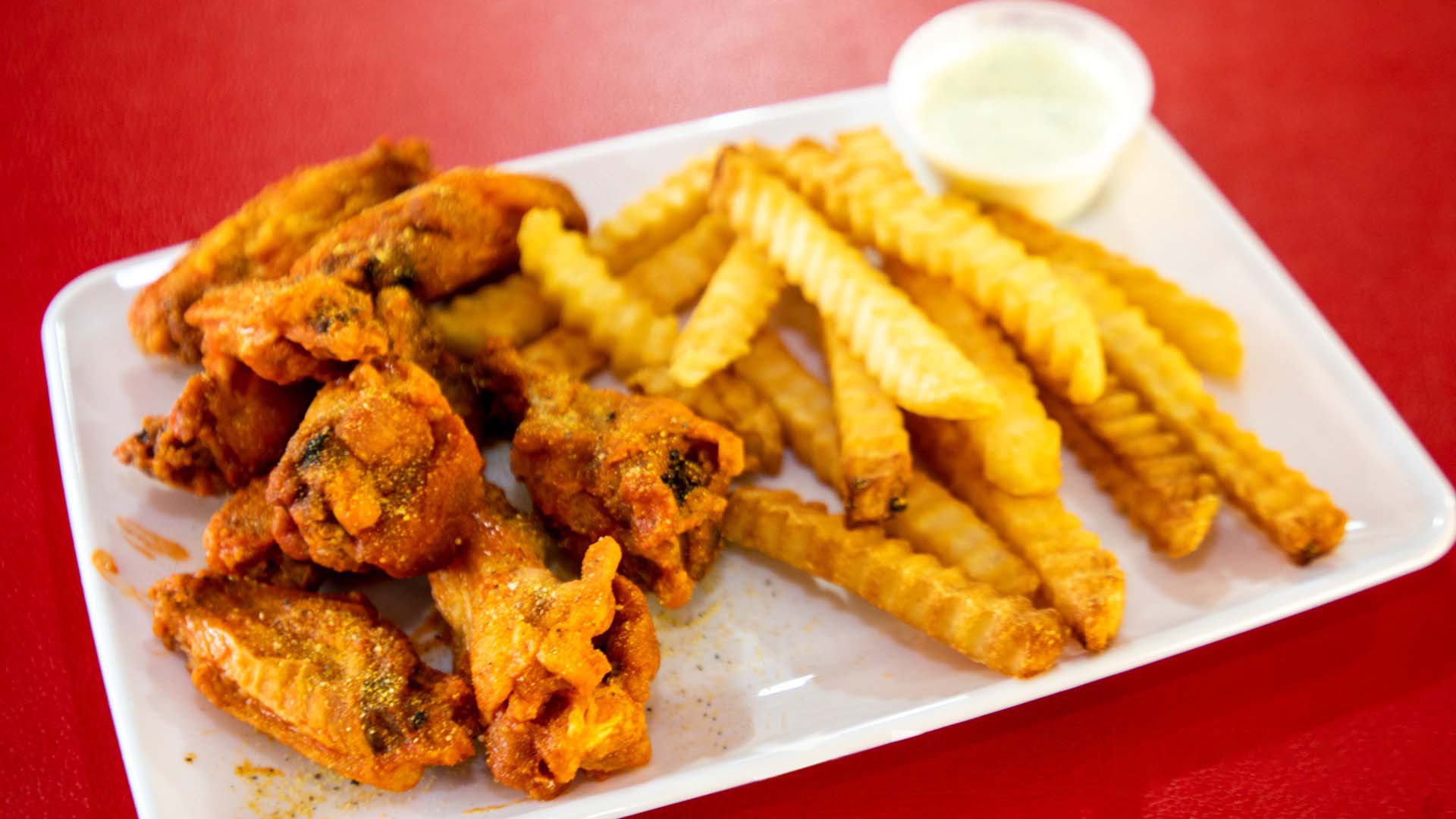 A plate of fried chicken wings with crinkle-cut fries and a side of dipping sauce on a red table.