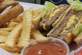 A cheeseburger with lettuce and tomatoes, fries, onion rings, and a side of ketchup.