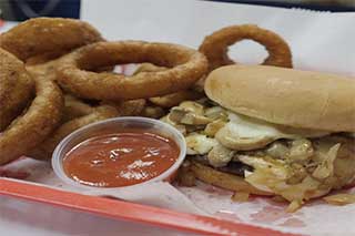 Plate of onion rings with a chicken sandwich and a side of dipping sauce.