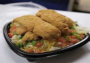 A plate containing a salad topped with breaded chicken cutlets.