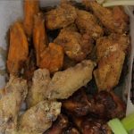 Assorted 70 wings with celery sticks in a takeout box.