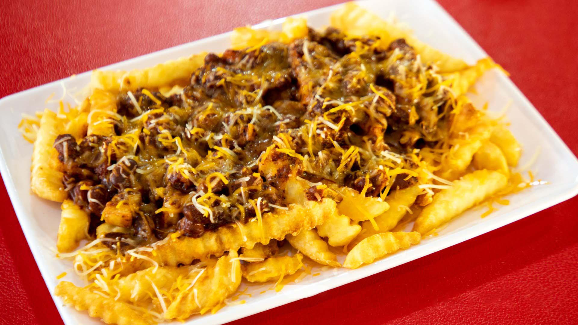 A plate of fries topped with shredded cheese and chili con carne on a red table.