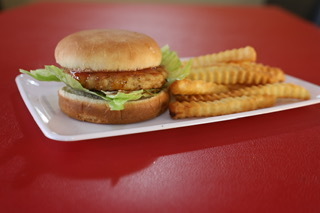 A chicken sandwich with lettuce on a bun and a side of crinkle-cut fries on a white plate.