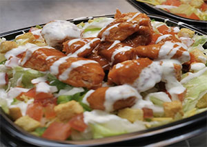 A buffalo chicken salad with croutons and drizzled dressing.