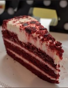 A slice of red velvet cake with cream cheese frosting on a plate.