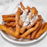 A plate of golden-brown churros dusted with powdered sugar.