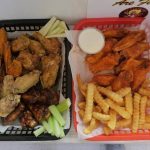Two baskets of assorted chicken wings with sides of celery and french fries.