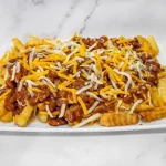A plate of crinkle-cut fries topped with chili and shredded cheddar cheese.
