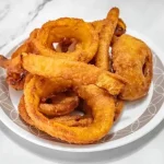Plate of crispy fried onion rings on a marble surface.