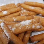 A pile of freshly dusted churros on a plate.