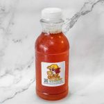 Bottle of red hot sauce on a marble surface.