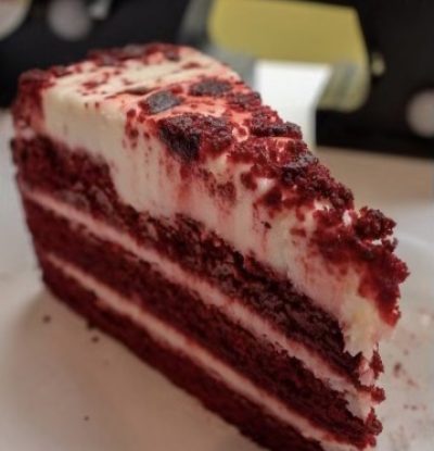 A slice of red velvet cake with cream cheese frosting on a plate.