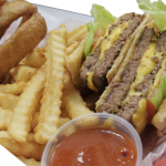 A cheeseburger with lettuce and tomatoes, served with a side of fries, onion rings, and a small container of ketchup.