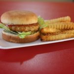 A chicken sandwich with lettuce on a bun and a side of crinkle-cut fries on a white plate.
