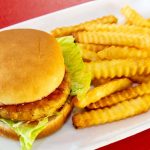 A chicken sandwich and crinkle-cut fries served on a white plate.